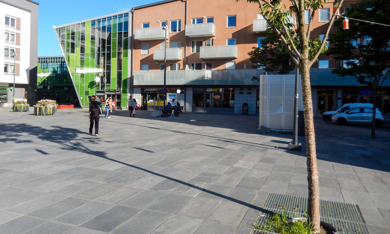Torg i en stadsdel. Ett par människor rör sig på den öppna ytan.