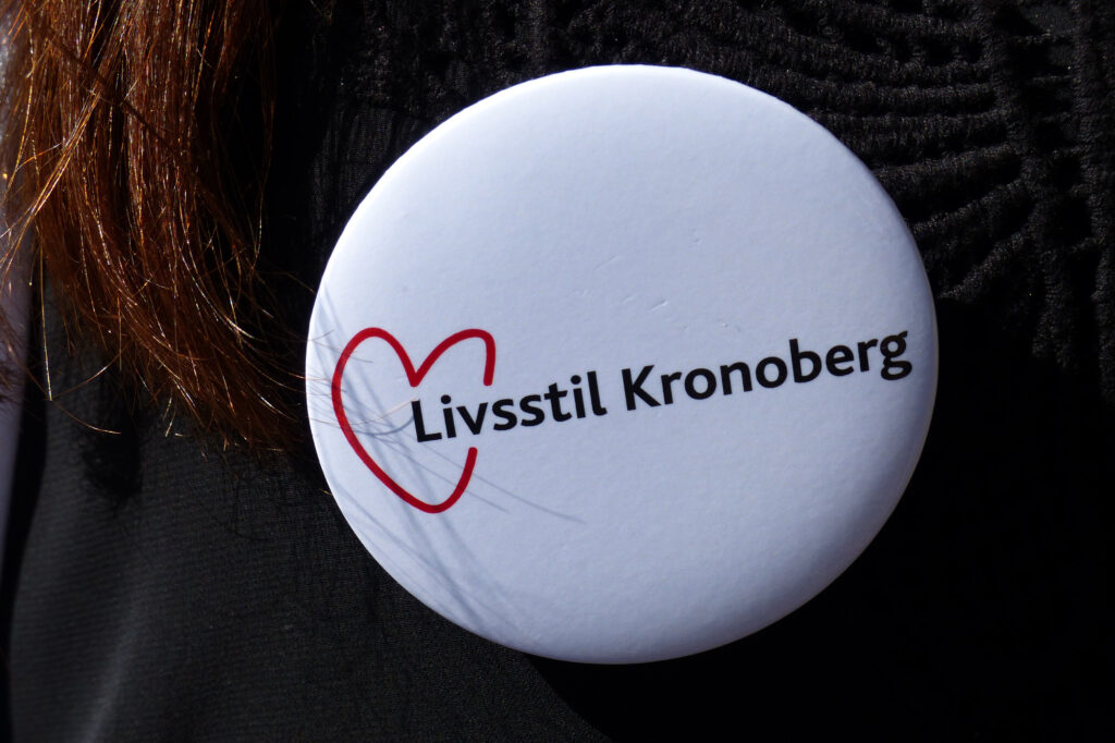 Fastnålad knapp med texten Livsstil Kronoberg på en tröja.